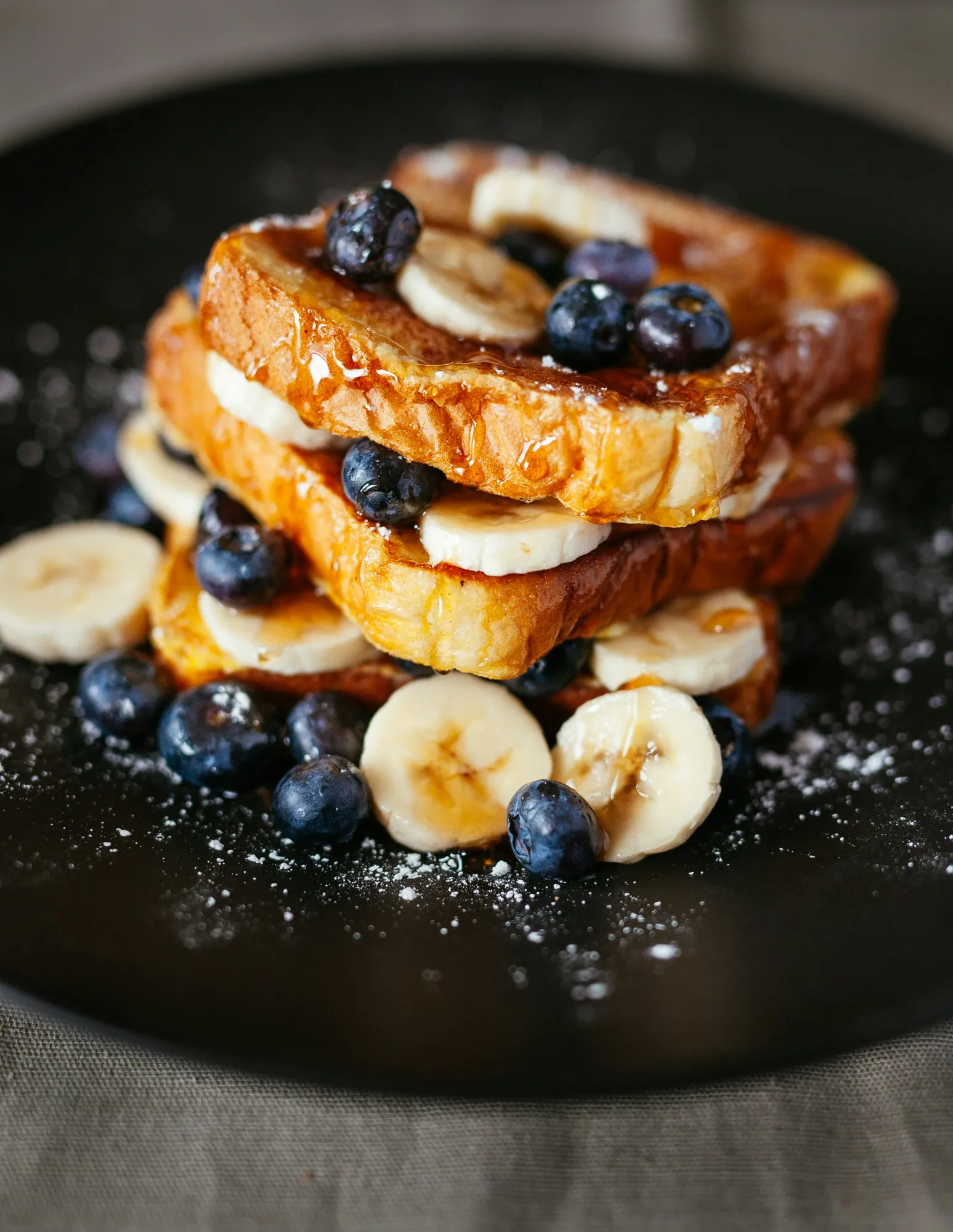 A black plate topped with bananas and blueberries.