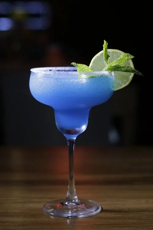 A blue cocktail with a lime garnish on the rim.