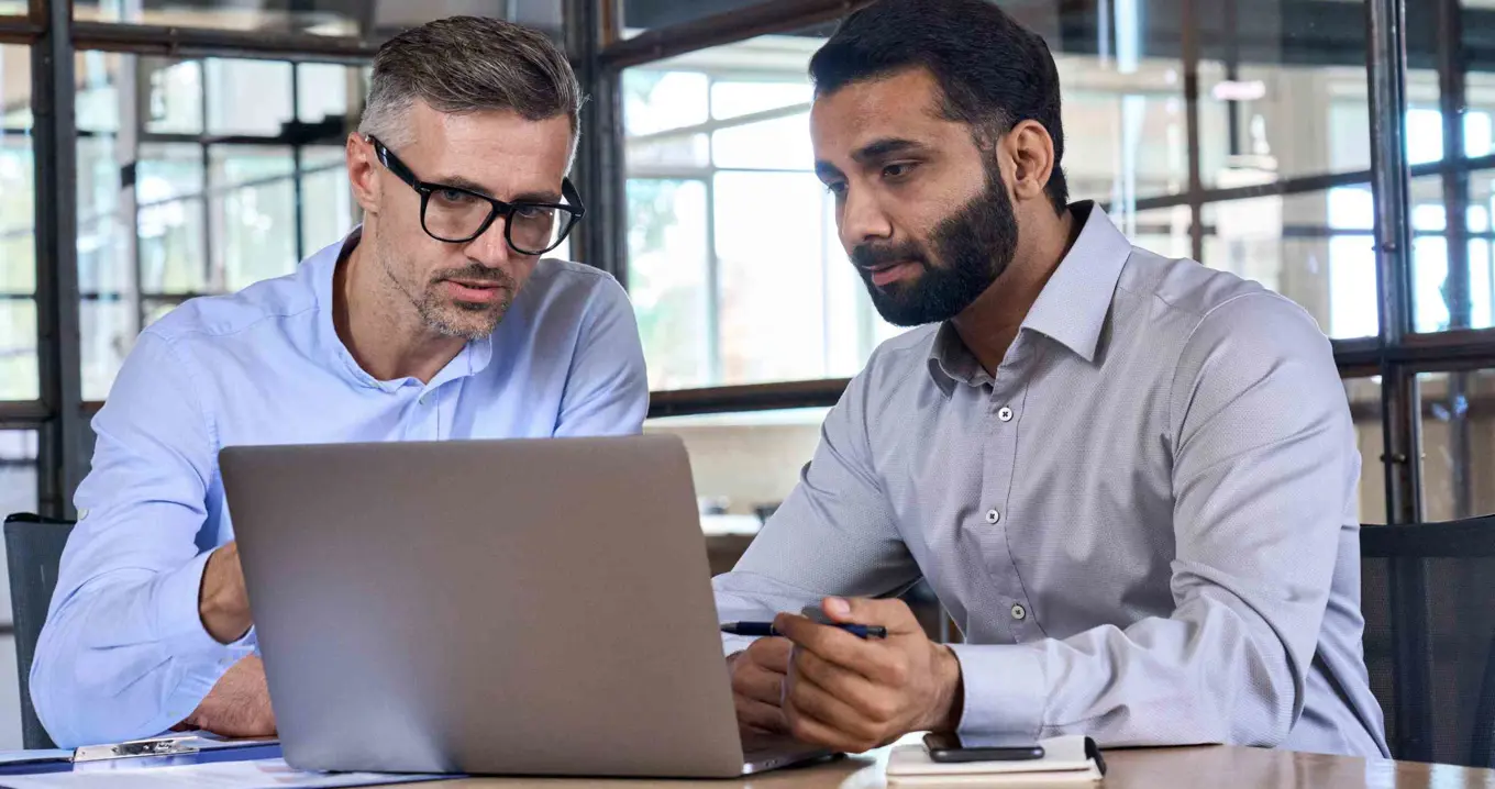 Två kollegor i diskussion vid dator – illustrerar affärsrådgivning och strategiskt beslutsstöd i digital miljö.