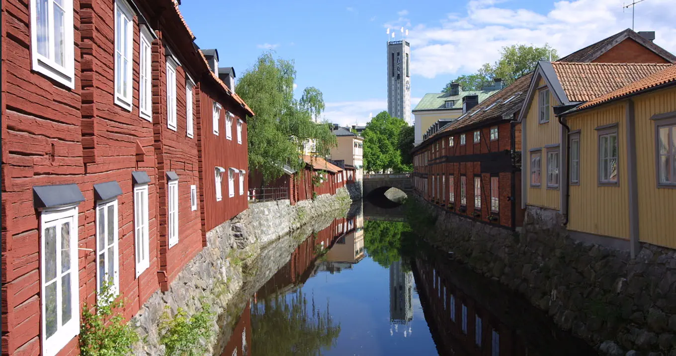 Illustration av Västerås stad med traditionella trähus längs Svartån och höghuset Skrapan i bakgrunden – symboliserar kommunal utveckling och digitalisering av budgetprocesser.