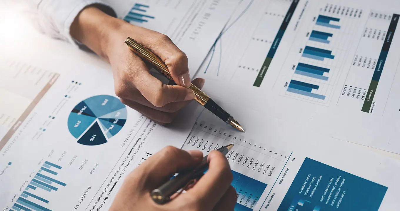 Två personer analyserar rapporter med stapeldiagram, cirkeldiagram och tabeller.