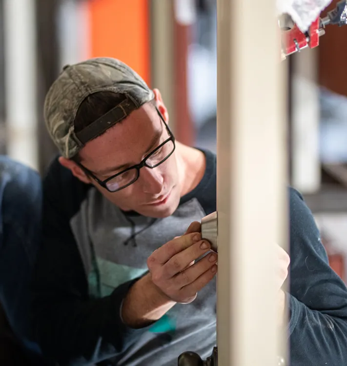Man wearing glasses and a backwards cap installing door lock hardware