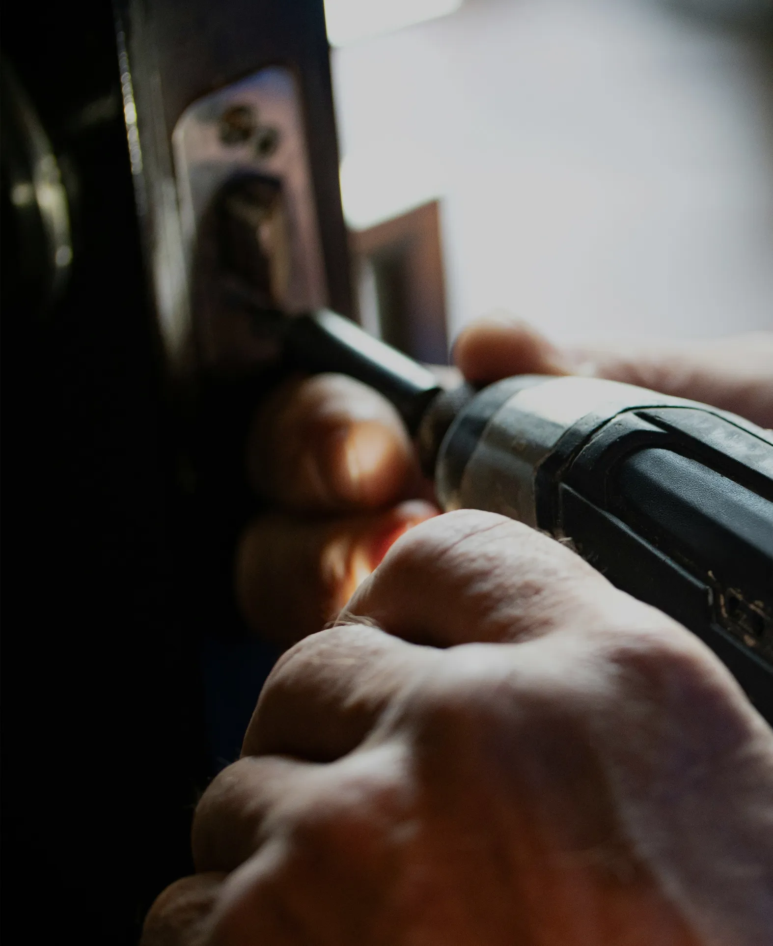 Close-up of hands using a power screwdriver to fix a door lock.