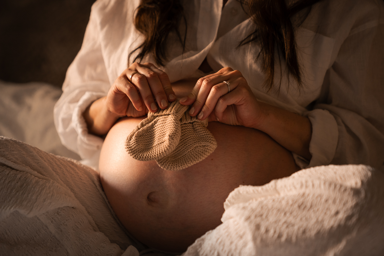 Detailaufnahme Babybauch mit Babyschuhen – Schwangere hält kleine gestrickte Babysöckchen auf dem Bauch, symbolträchtige Babybauchfotografie mit emotionaler Bedeutung.