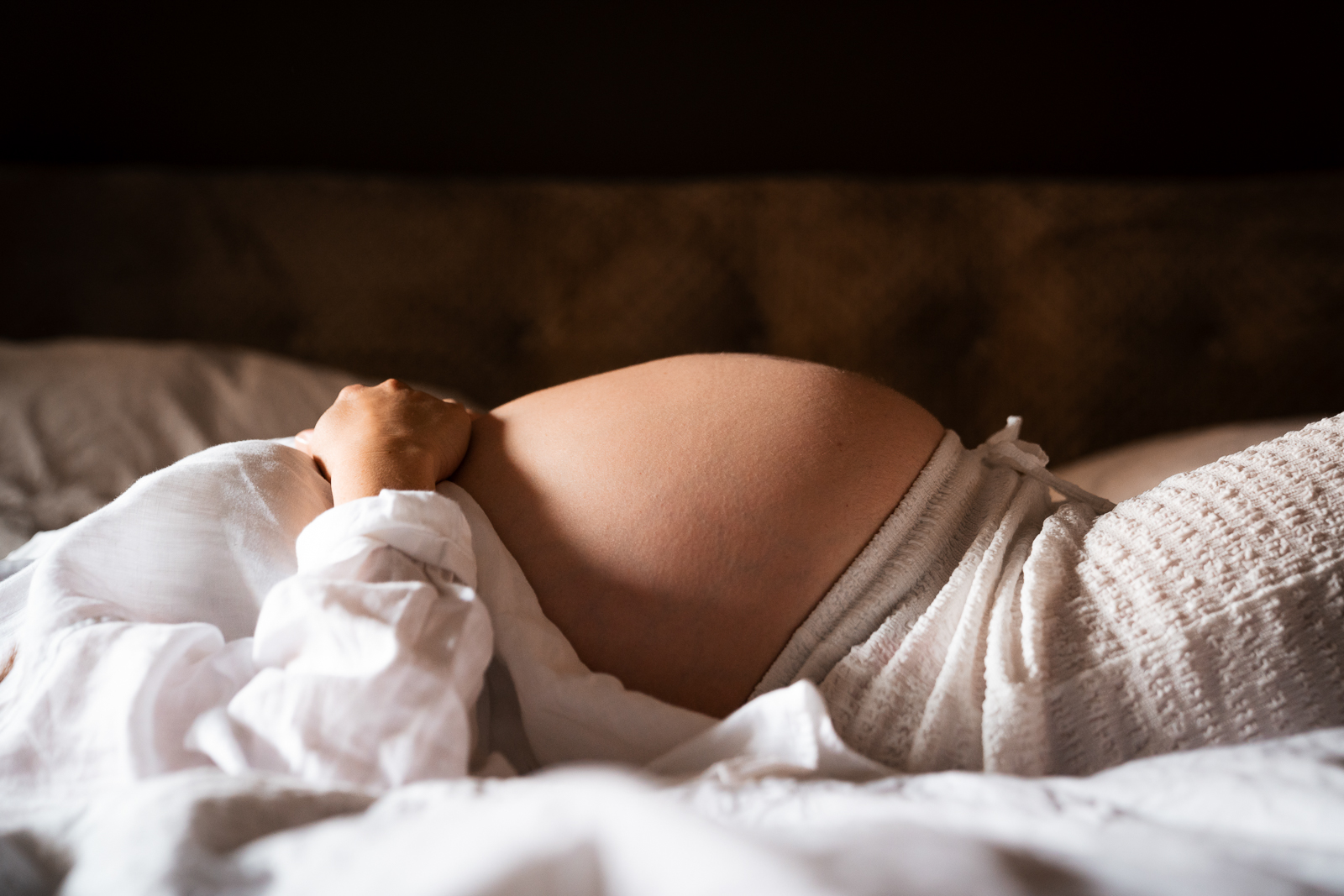 Schwangerschaftsfoto im Liegen – seitliche Perspektive des runden Babybauchs im warmen Licht, intime und ruhige Babybauchfotografie.