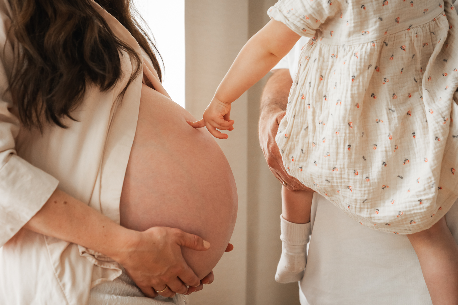 Babybauch Shooting mit Geschwisterkind – Kleinkind berührt sanft den Bauch der schwangeren Mutter, emotionale Familienaufnahme in natürlichem Licht.