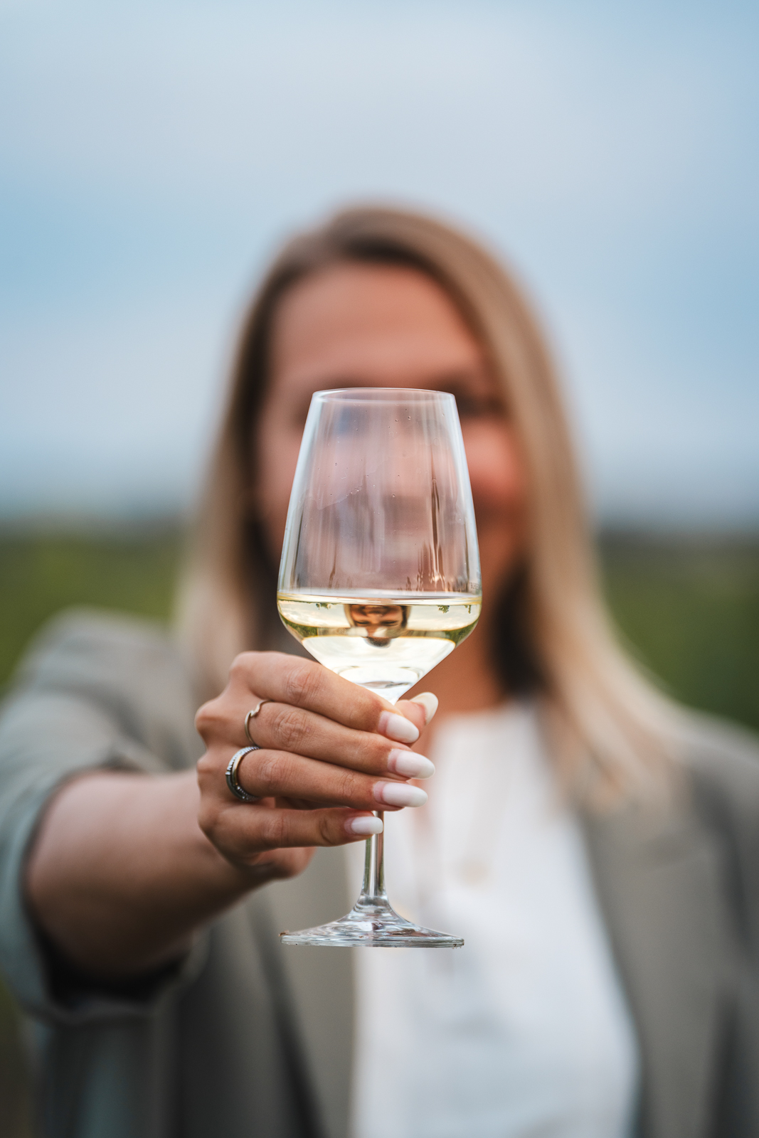 Frau hält ein Glas Weißwein vor die Kamera – Detailaufnahme im Weinberg