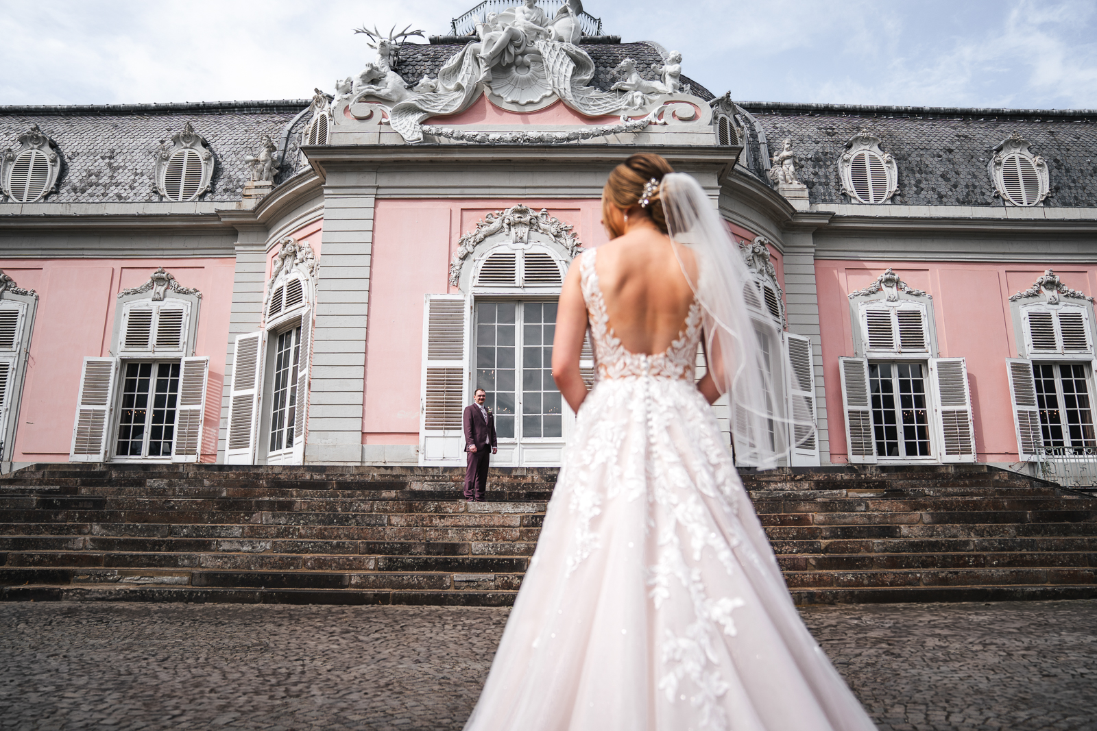 Braut im traumhaften Spitzenkleid schreitet die Treppen von Schloss Benrath hinauf zum Bräutigam | Hochzeitsfotograf Düsseldorf