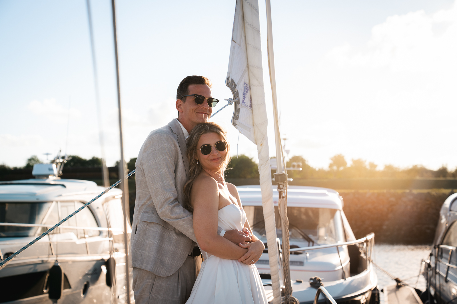 Brautpaar umarmt sich romantisch im Hafen auf einem Boot bei Sonnenuntergang, Editorial Hochzeitsfotografie