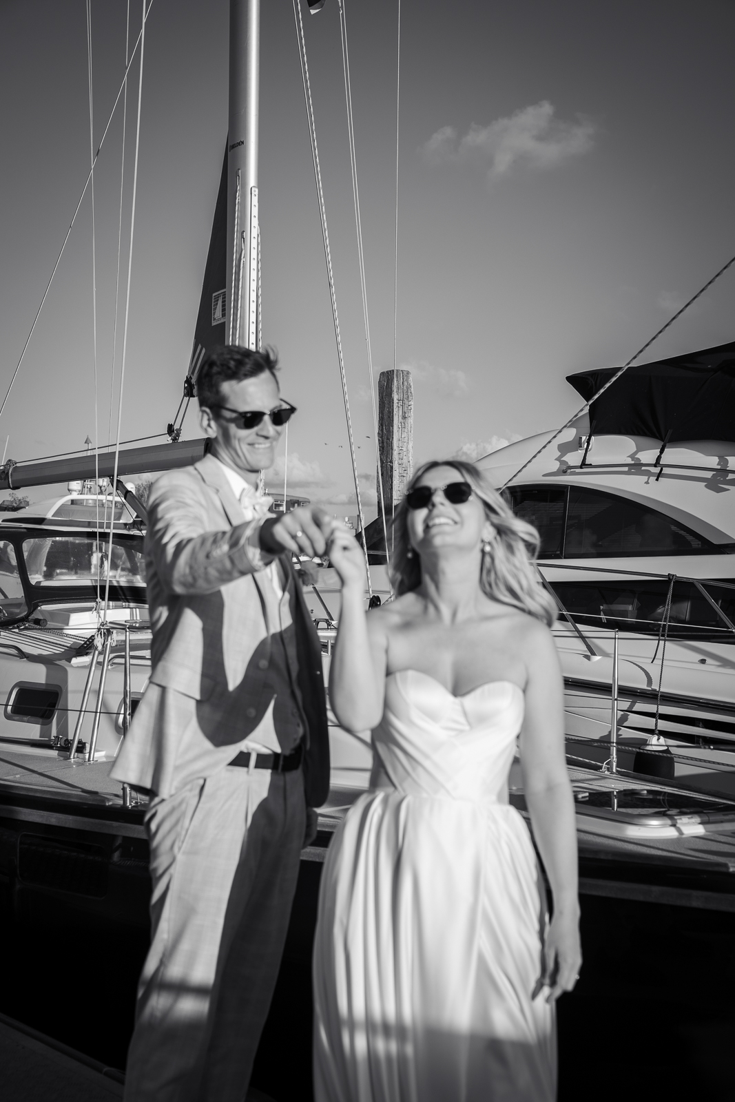 Schwarz-Weiß-Hochzeitsfoto: Braut und Bräutigam tanzen lachend und ausgelassen auf dem Steg am Hafen