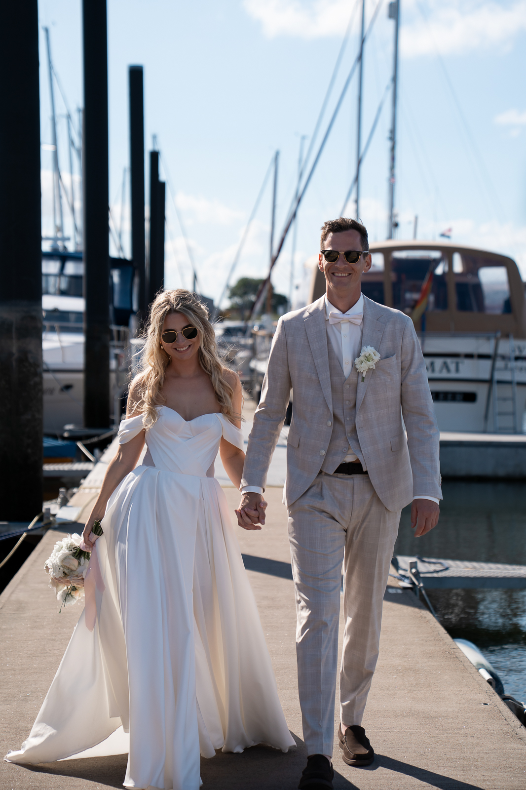 Braut und Bräutigam laufen Hand in Hand über einen Steg im Yachthafen, Editorial Hochzeitsfotografie auf Norderney