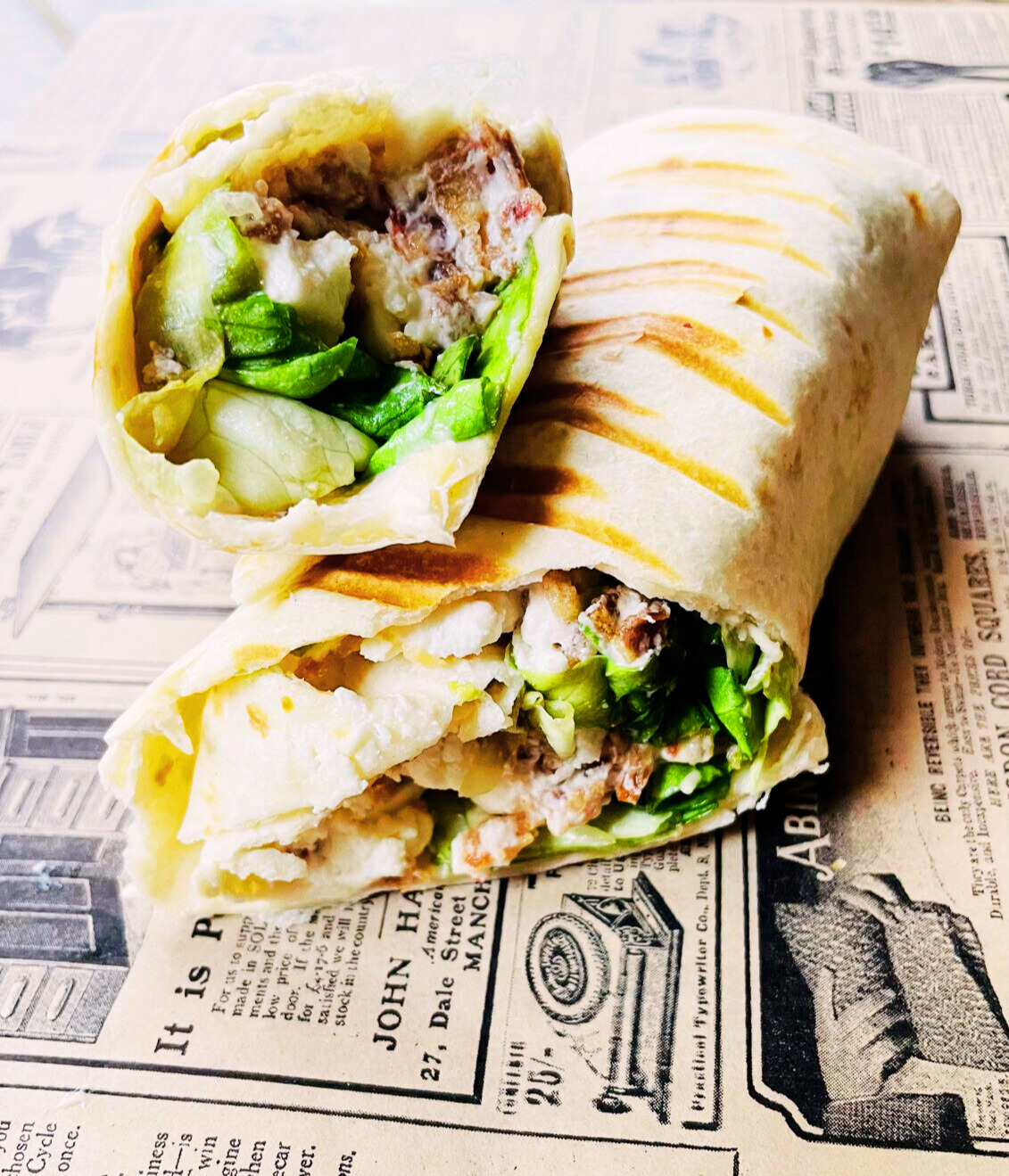 Deux wraps grillés coupés en deux, garnis de laitue, sauce blanche et morceaux de viande.