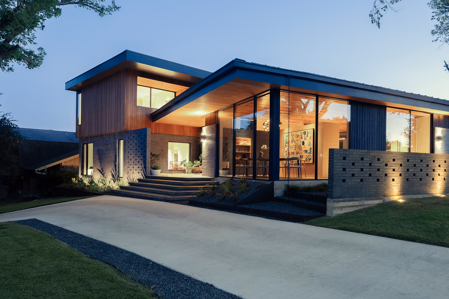 Elegant modern home exterior with expansive glass windows and inviting warm interior lighting.