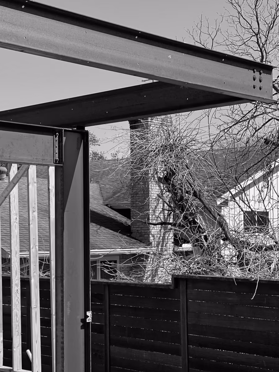 Residential outdoor landscape featuring a metal gate with a wooden fence surrounded by a tree.