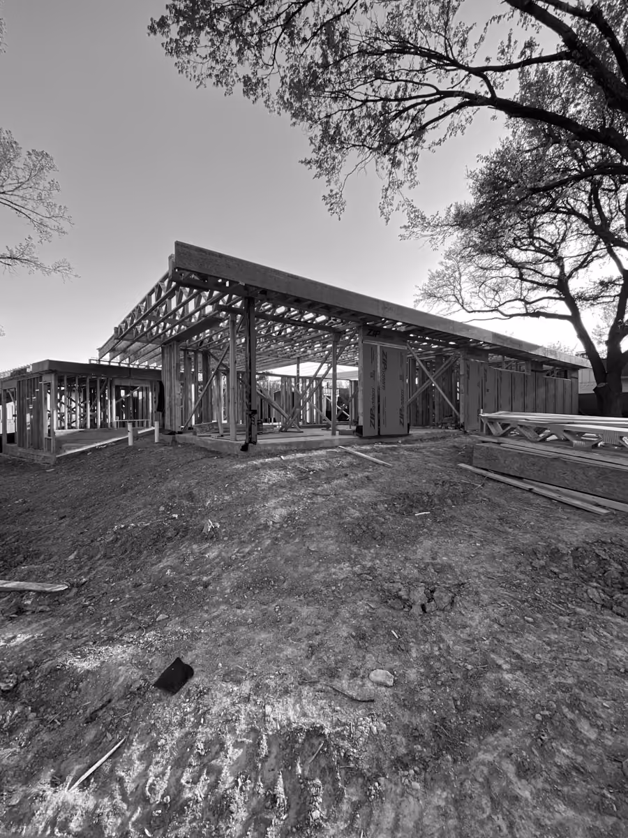 New home construction with wooden framing amidst a natural surroundings and dirt terrain.