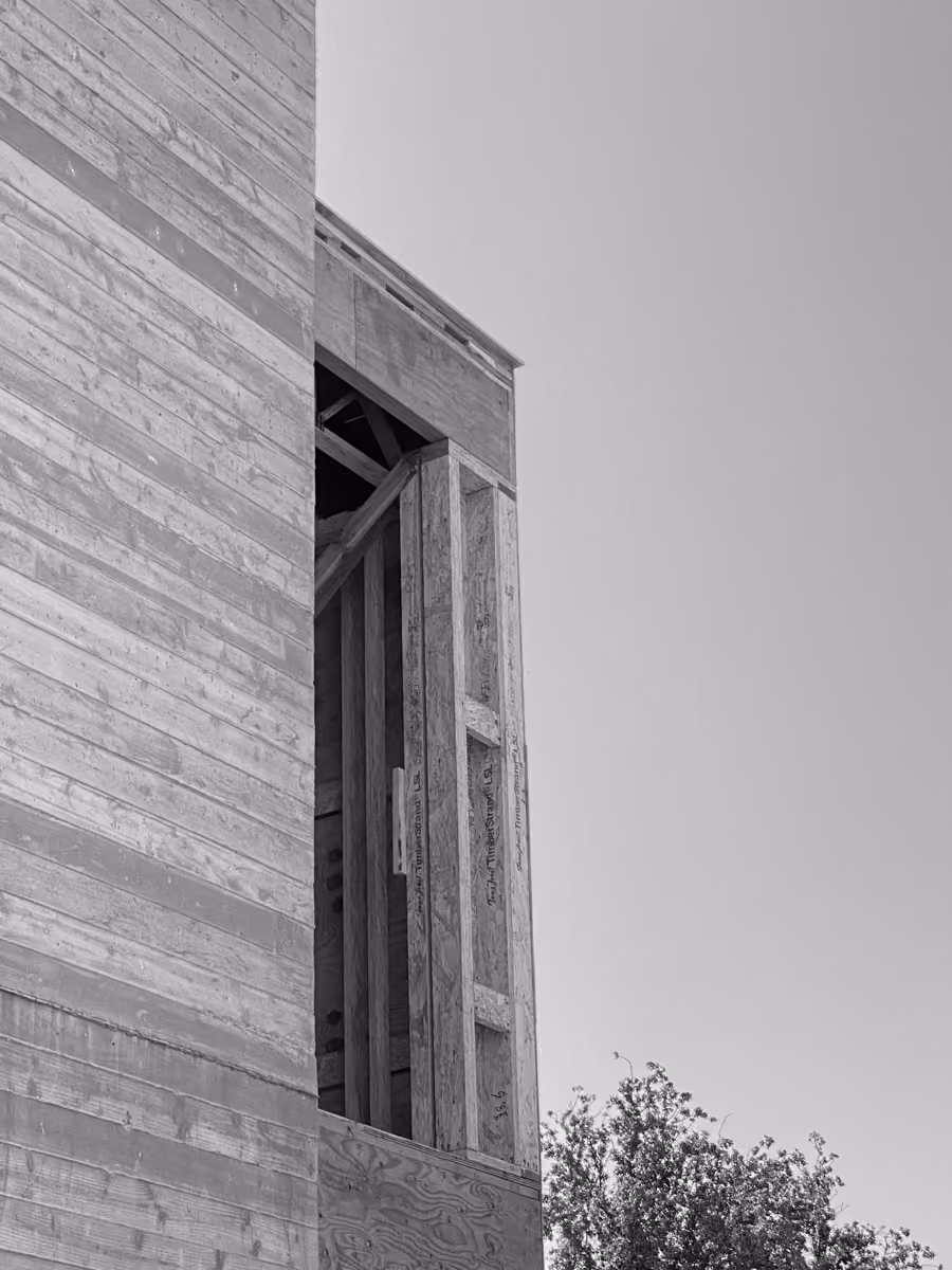 Wooden building structure with open frame on a construction site amidst lush green trees.