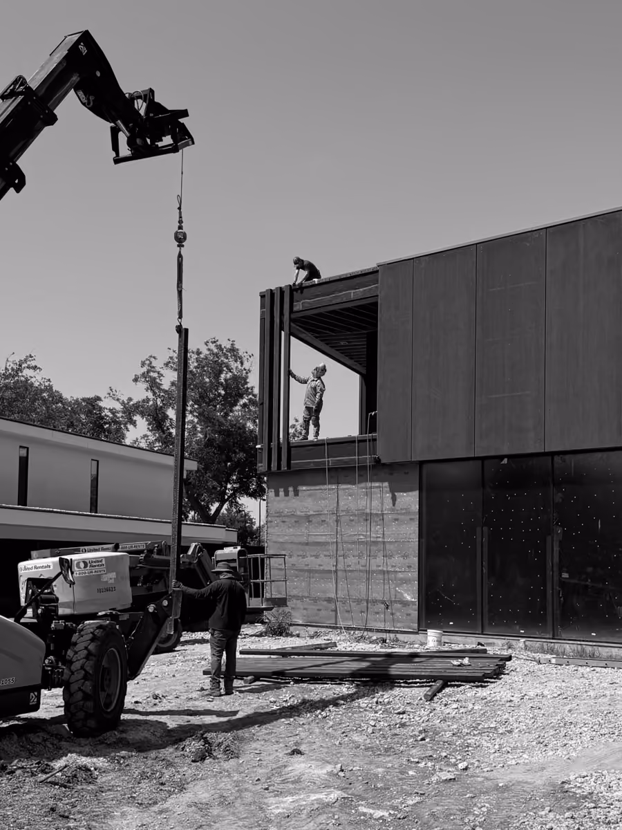 Construction workers assembling metal building panels outdoors with construction machinery and crane services.
