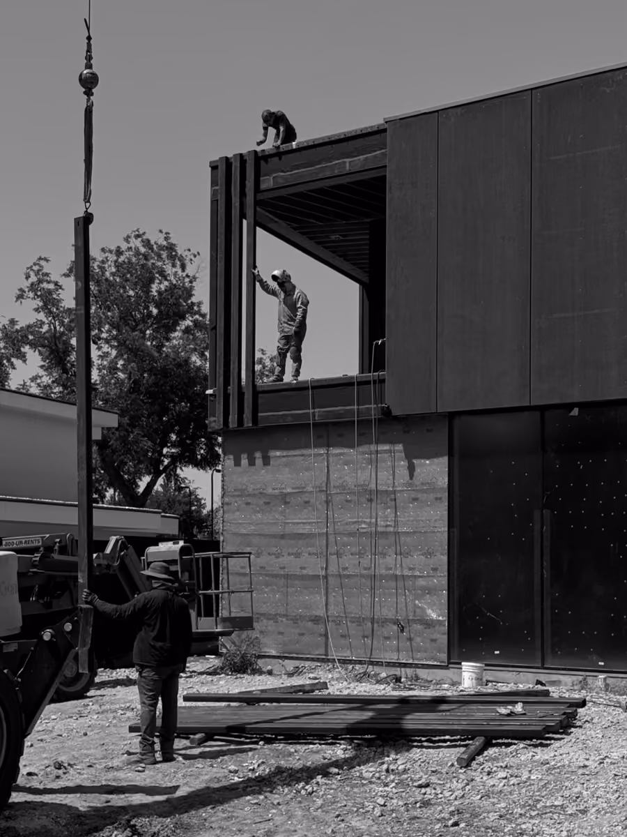 Construction workers assembling metal building panels on site with cranes and heavy equipment.