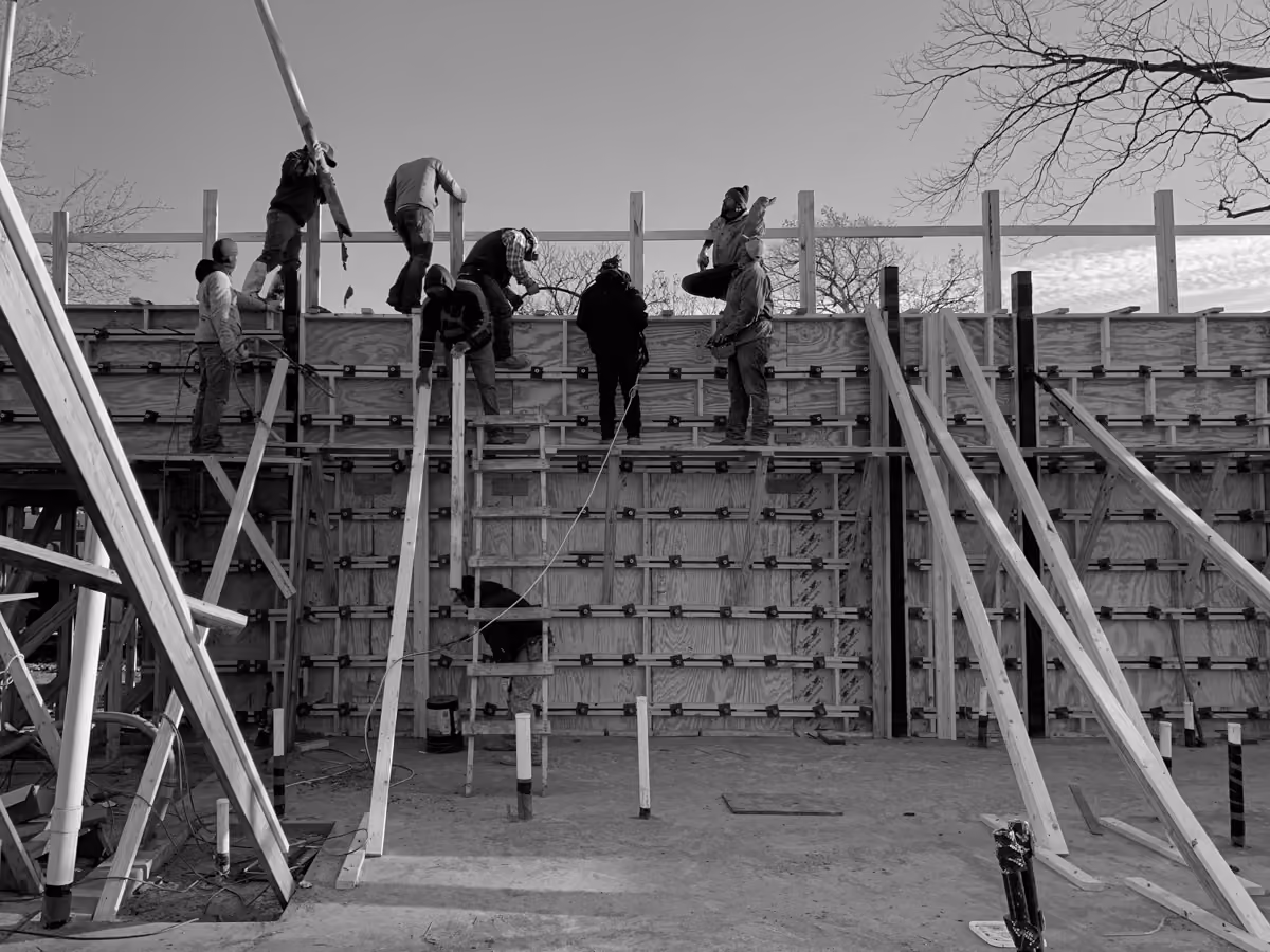 Skilled construction workers build wall formwork with natural wood and steel scaffolding equipment outdoors safely.