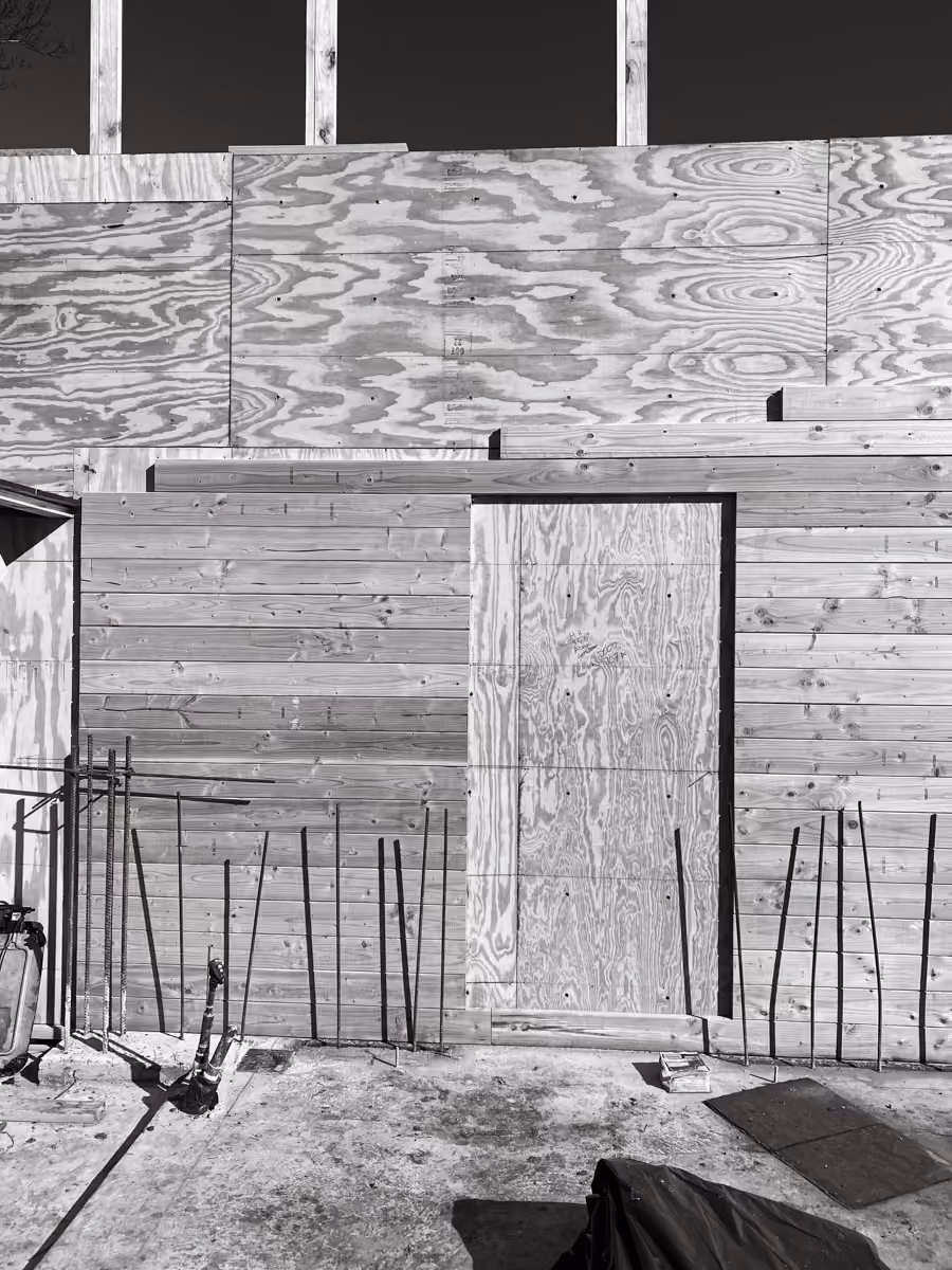 Wooden wall with construction-site rebar, tools, and door frame in progress.