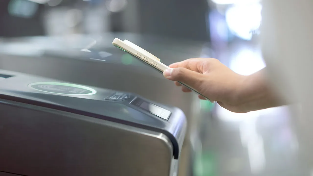 Hand hält ein Smartphone nahe an das Lesegerät eines kontaktlosen Zahlungsterminals.