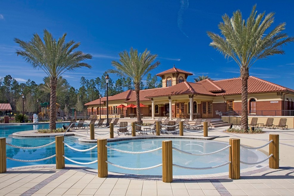 Resort pool with palm trees and clubhouse under bright blue sky