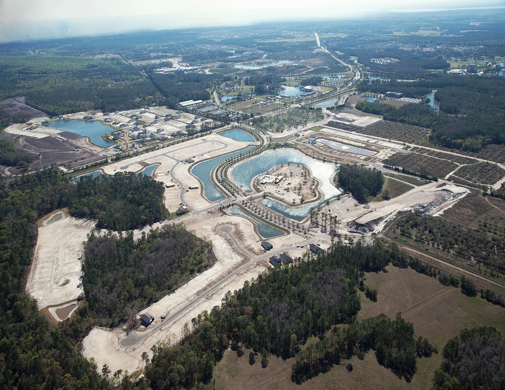 Aerial view of large construction site with water features and surrounding forest