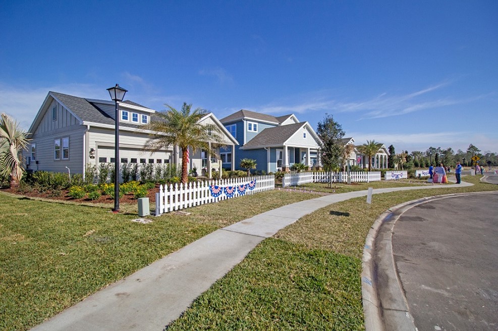 Suburban neighborhood with white picket fences, palm trees, and blue sky