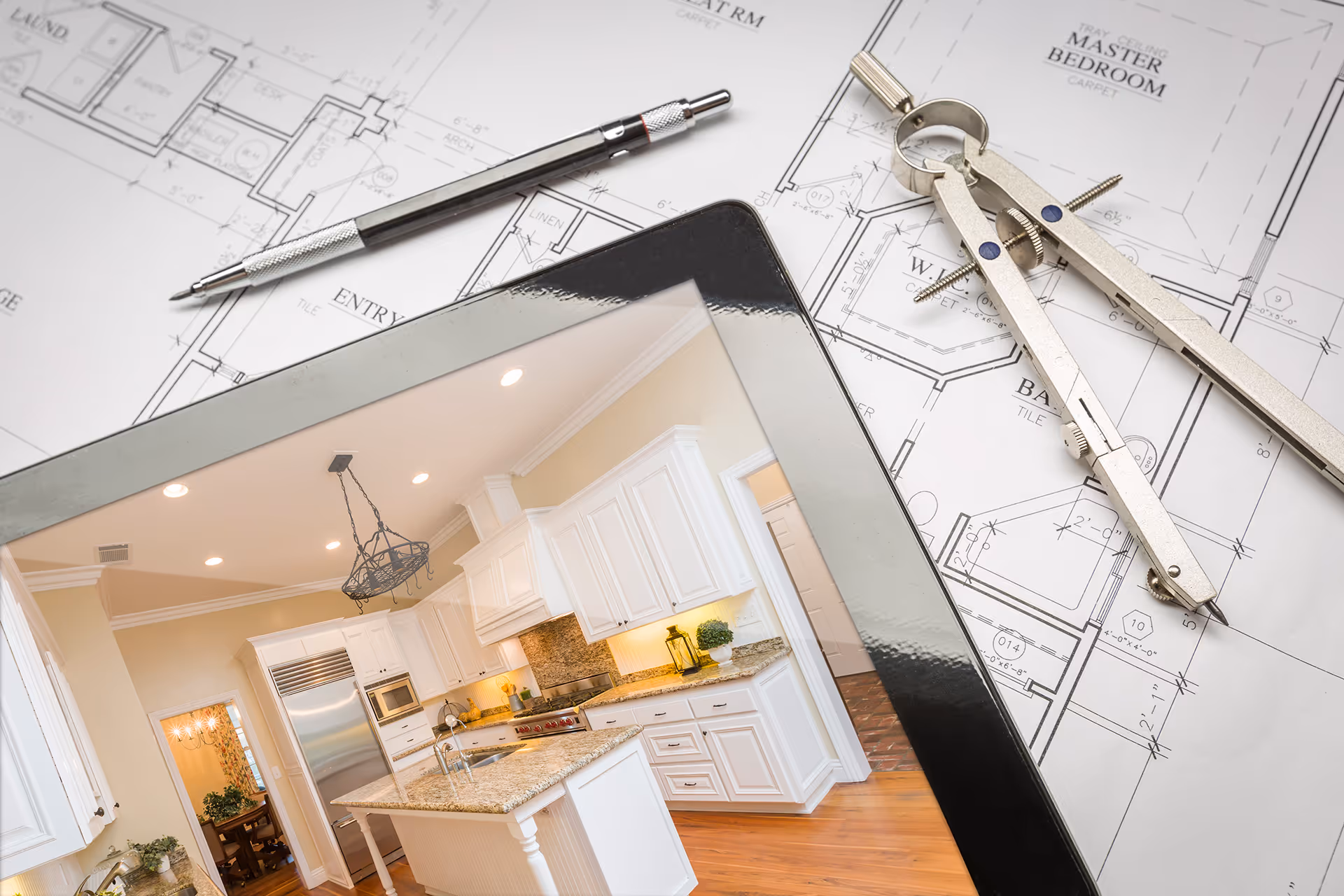 Tablet showing modern kitchen with granite countertops on top of architectural floor plans with drafting tools.
