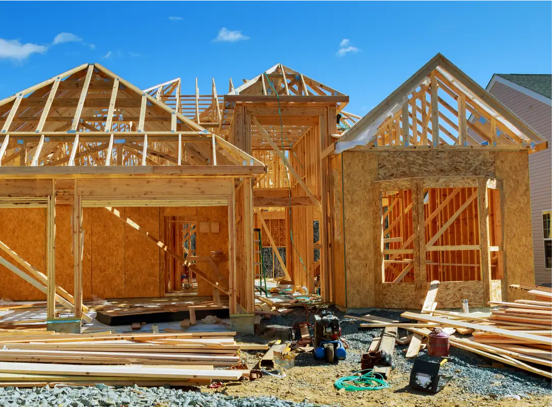Residential house under construction featuring exposed wooden framing roofing trusses and scattered building materials on site