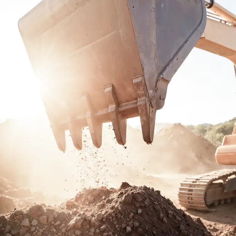 Excavator bucket dropping soil at a construction site in bright sunlight
