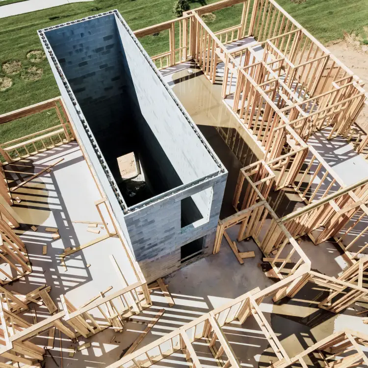 Aerial view of residential construction site showing wooden framing and a central concrete structure on a poured foundation