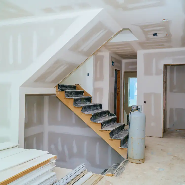 Interior under construction with drywall installed and stairs partially covered for protection