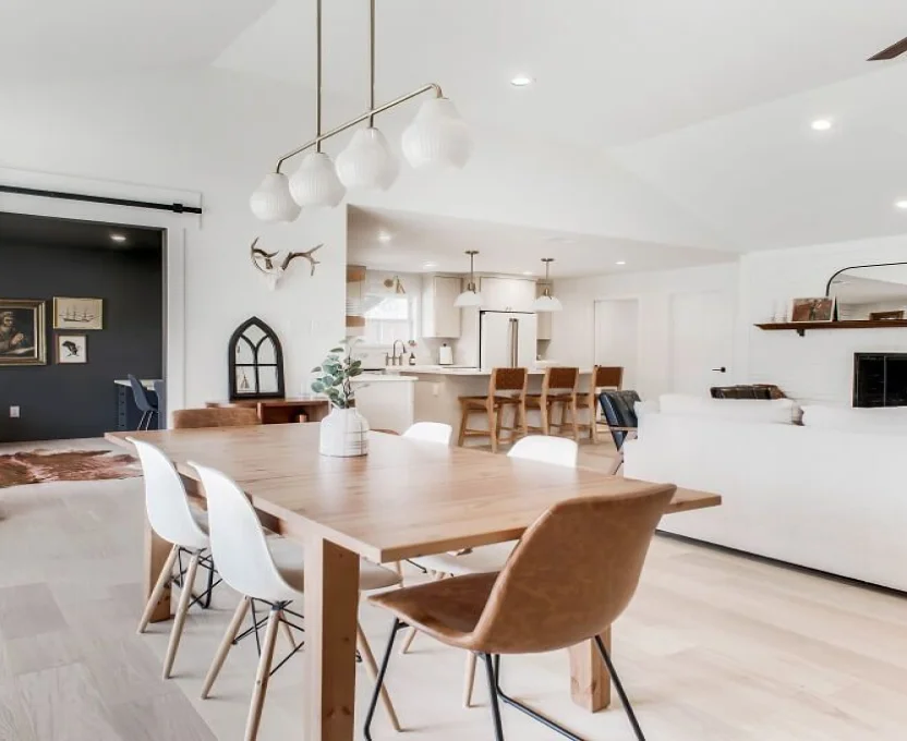 Bright open-concept interior with wood dining table modern lighting and white kitchen in the background