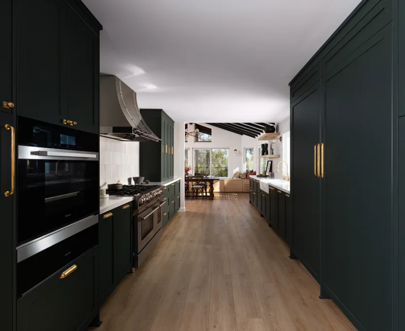 Sleek galley kitchen with dark cabinets gold hardware wood floors and view into dining area