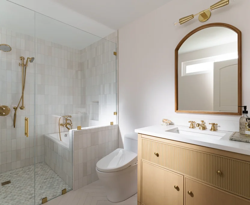 Elegant bathroom with light wood vanity gold fixtures and glass-enclosed tub and shower combo