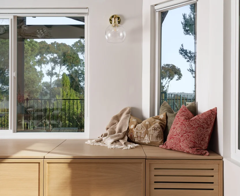 Cozy window nook with wood bench throw pillows and a view of trees outside