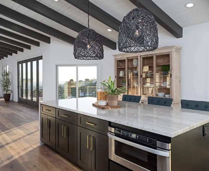 Kitchen with marble island dark cabinetry woven pendant lights and wood ceiling beams