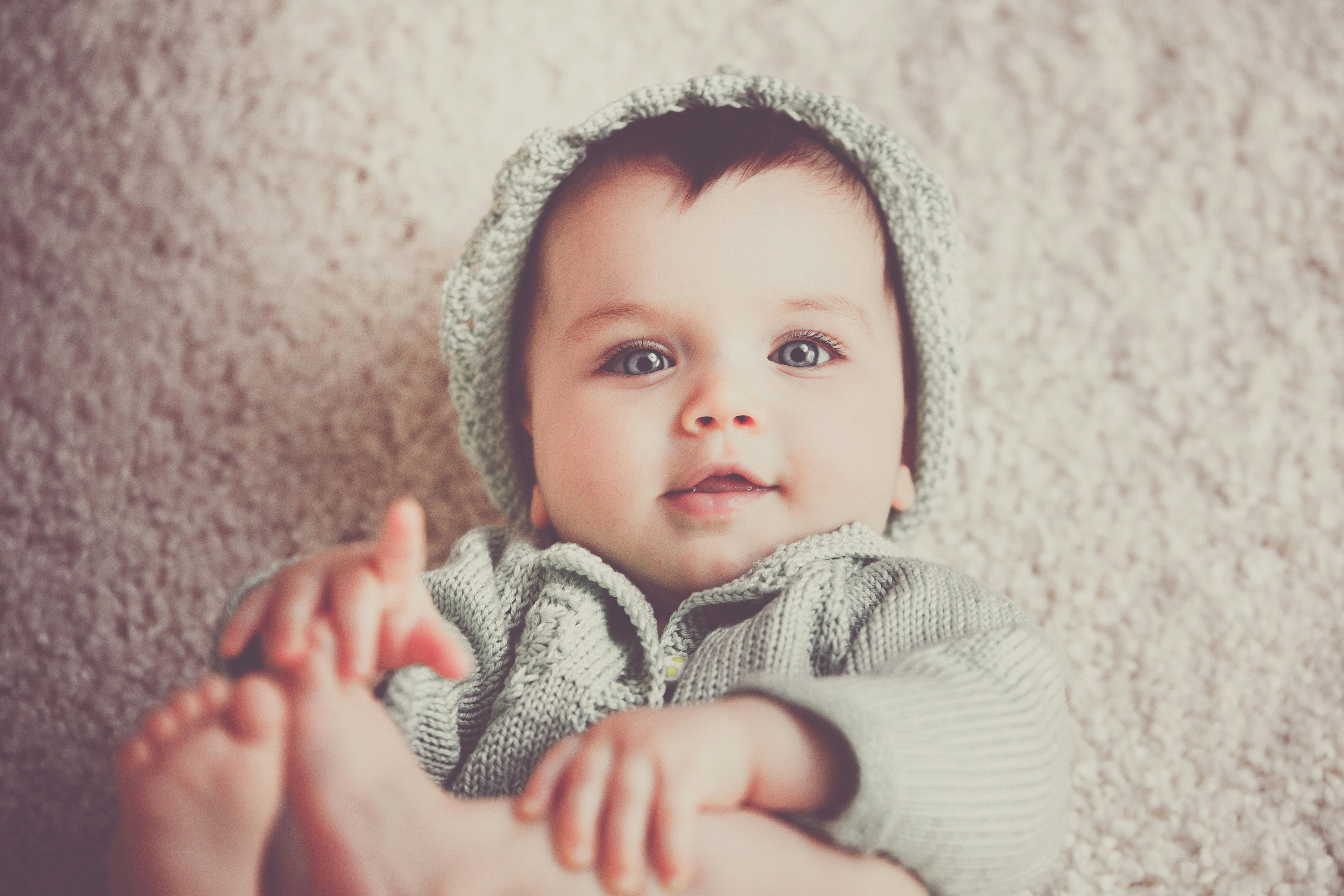 A baby with bright blue eyes looks into the camera, reaching for his feet.