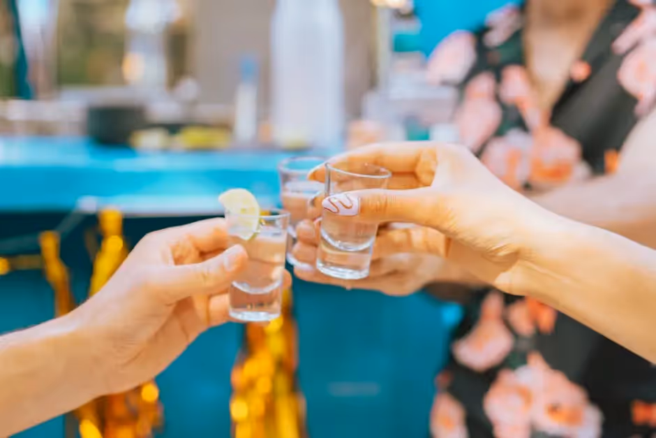 Close-up of people toasting with tequila shots in a festive outdoor setting.