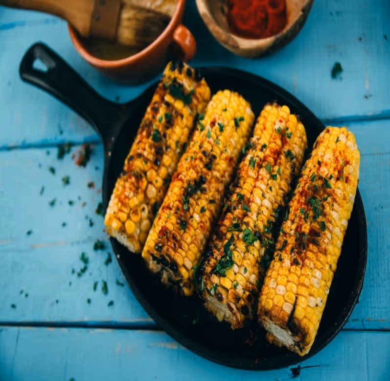 A black skillet with corn on the cob and a bowl of salsa.