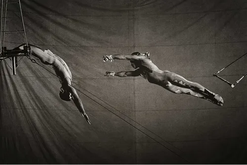 Two people in the middle of a trapeze jump.