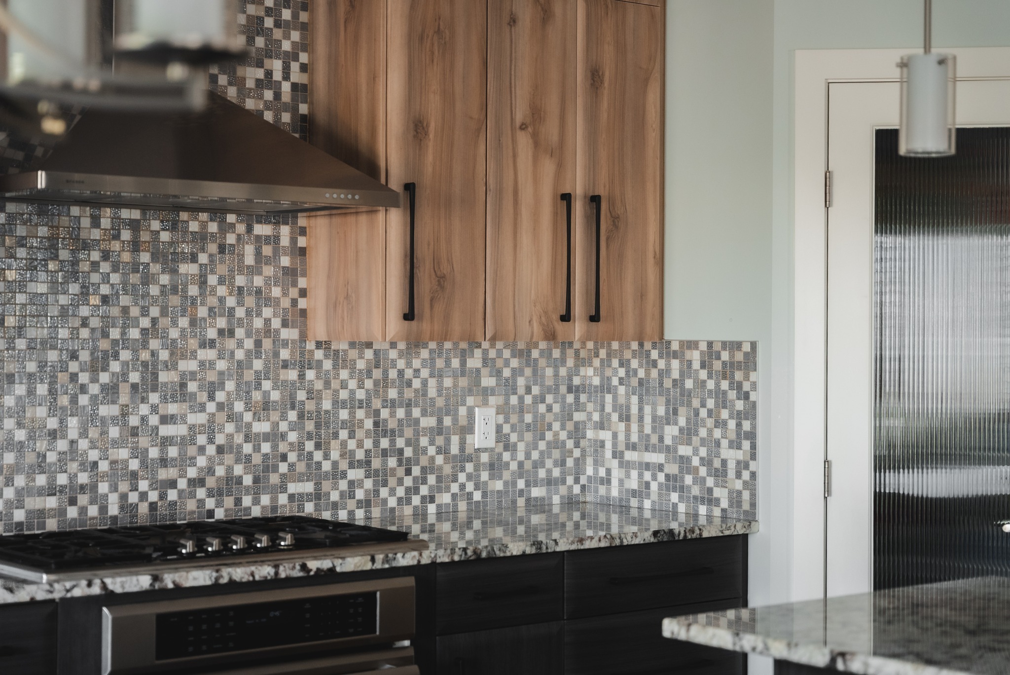 Modern kitchen with wood-grain cabinets, mosaic tile backsplash, and black hardware