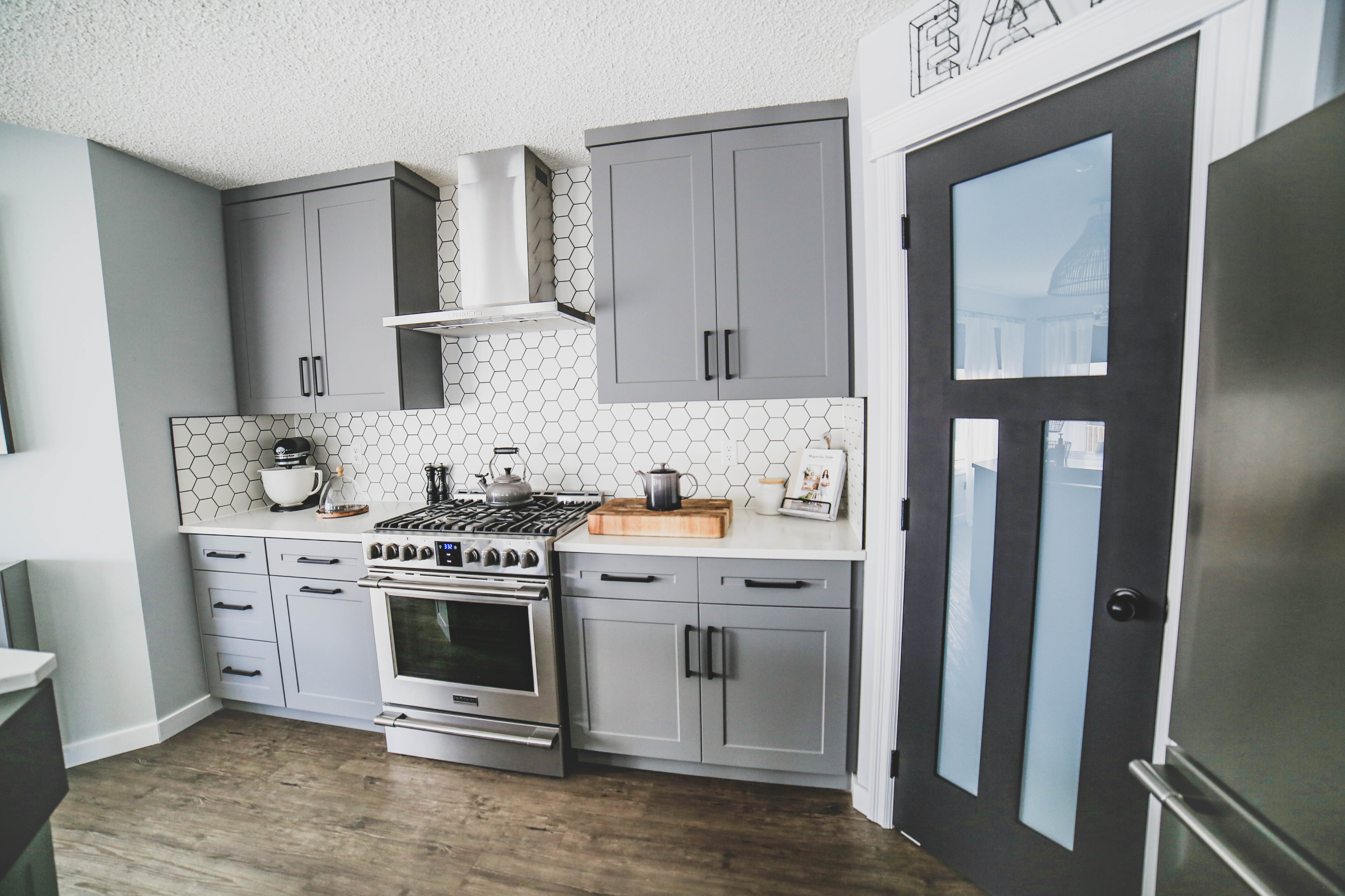 Modern kitchen with grey shaker cabinets, hexagon tile backsplash, and stainless steel range