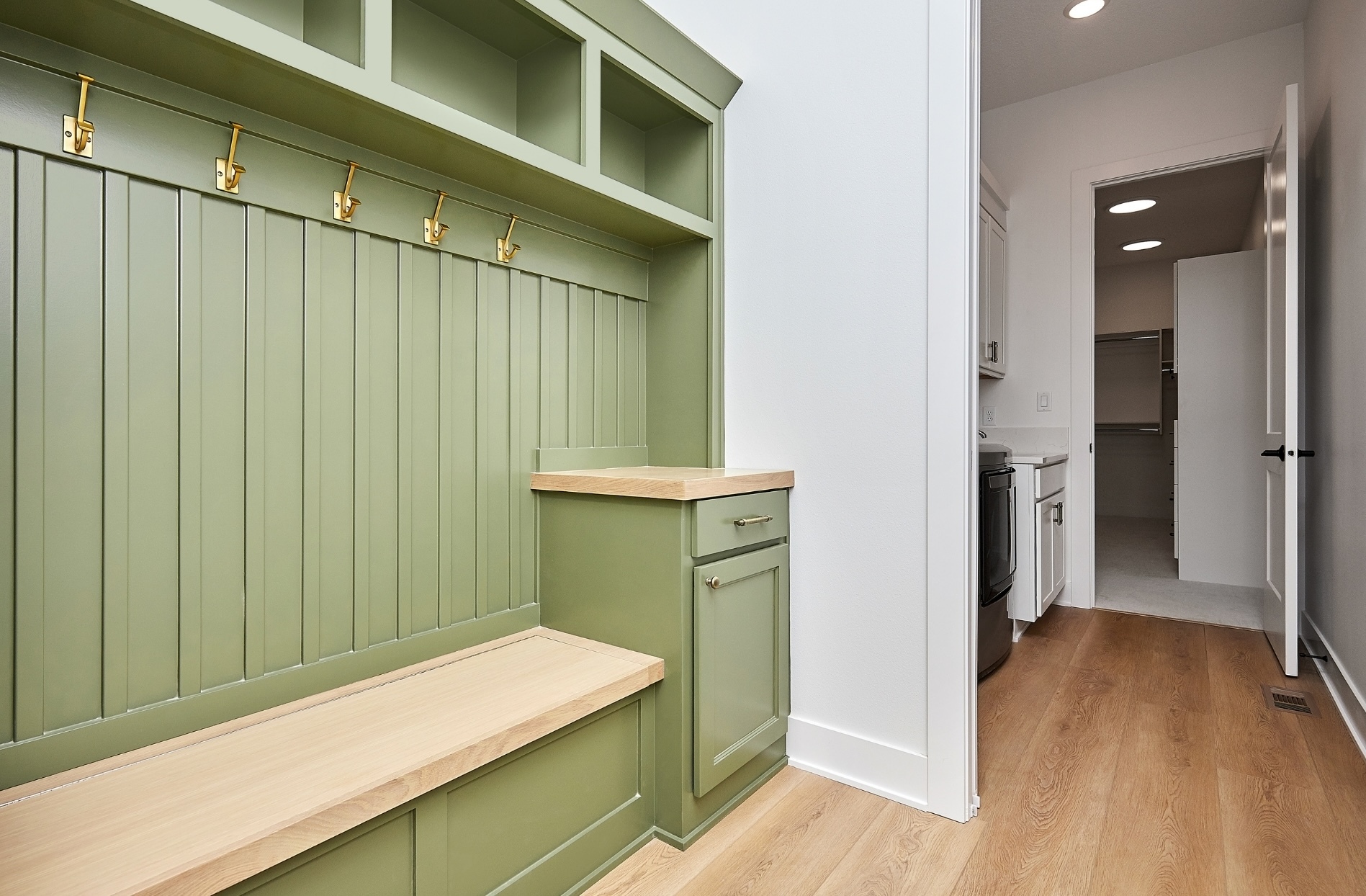 Sage green mudroom cabinets with a wood bench, brass hooks and open cubbies in an Edmonton back entry