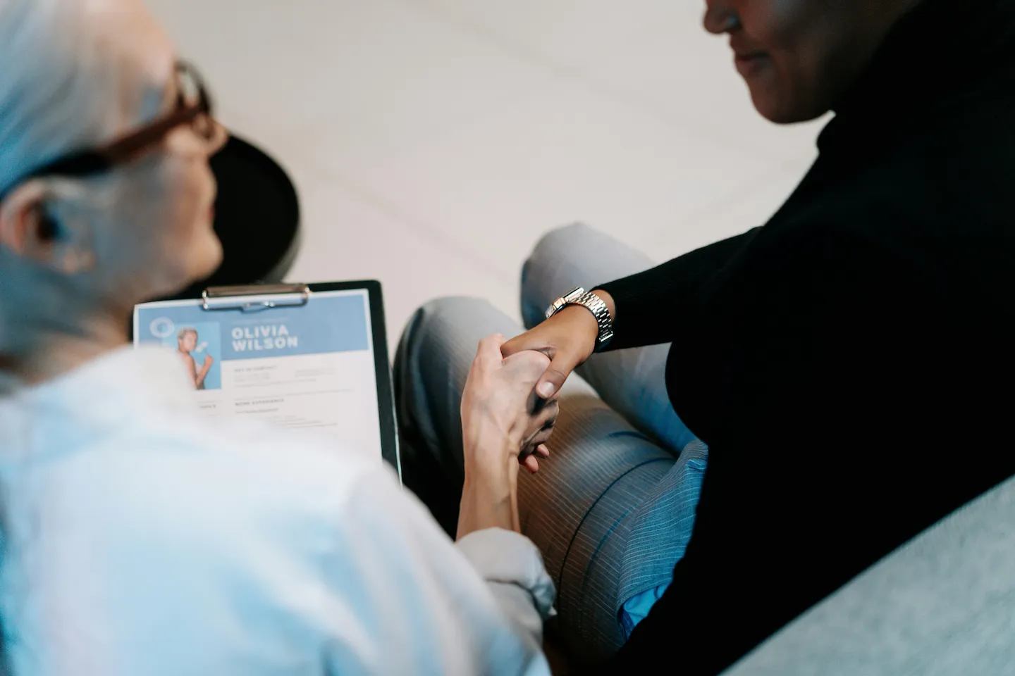 Two people sitting and shaking hands, one holding a clipboard with a document titled 'Olivia Wilson'.