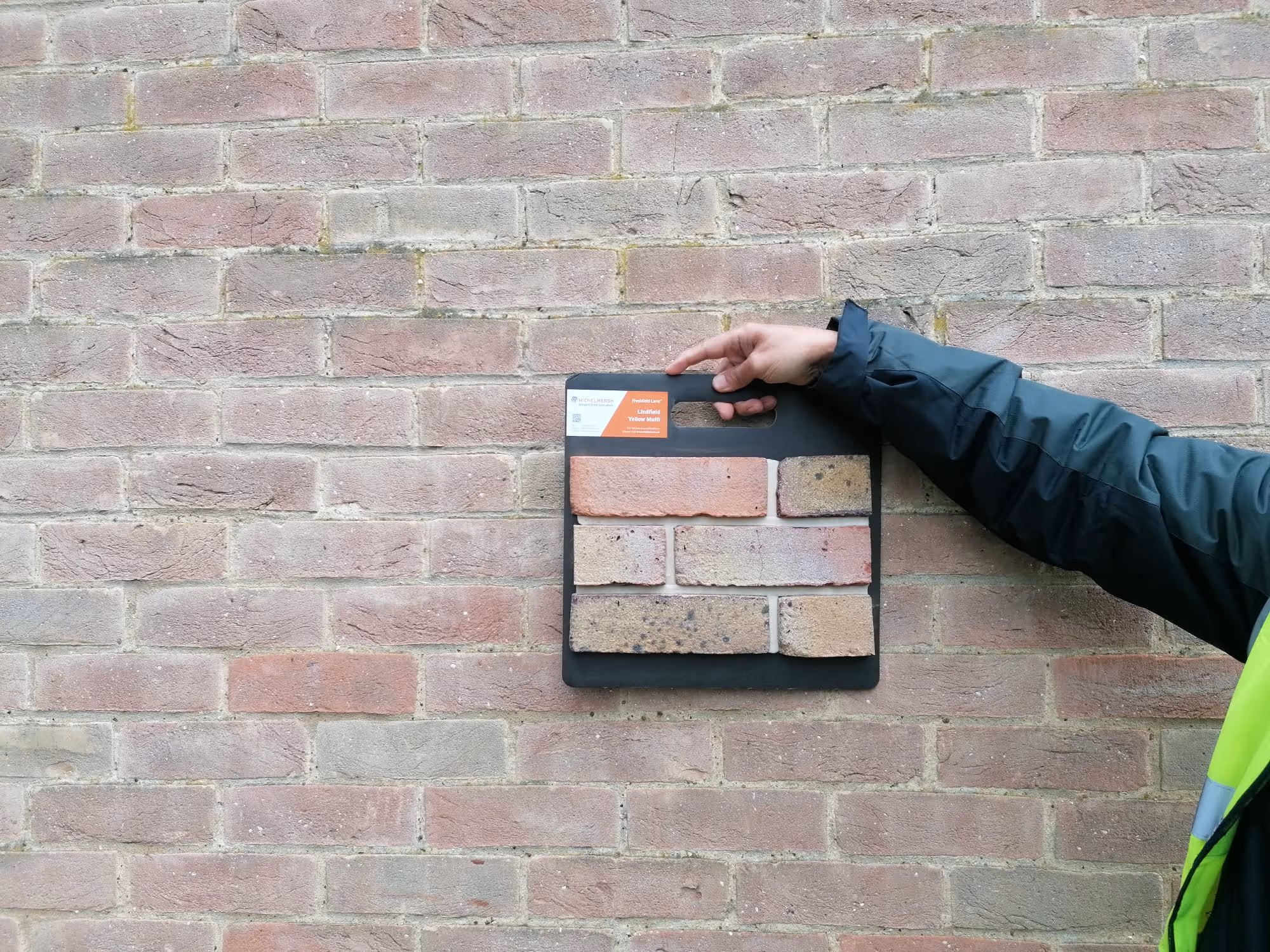 A Khandy's contractor holding a brick sample against a wall matching the colour and style