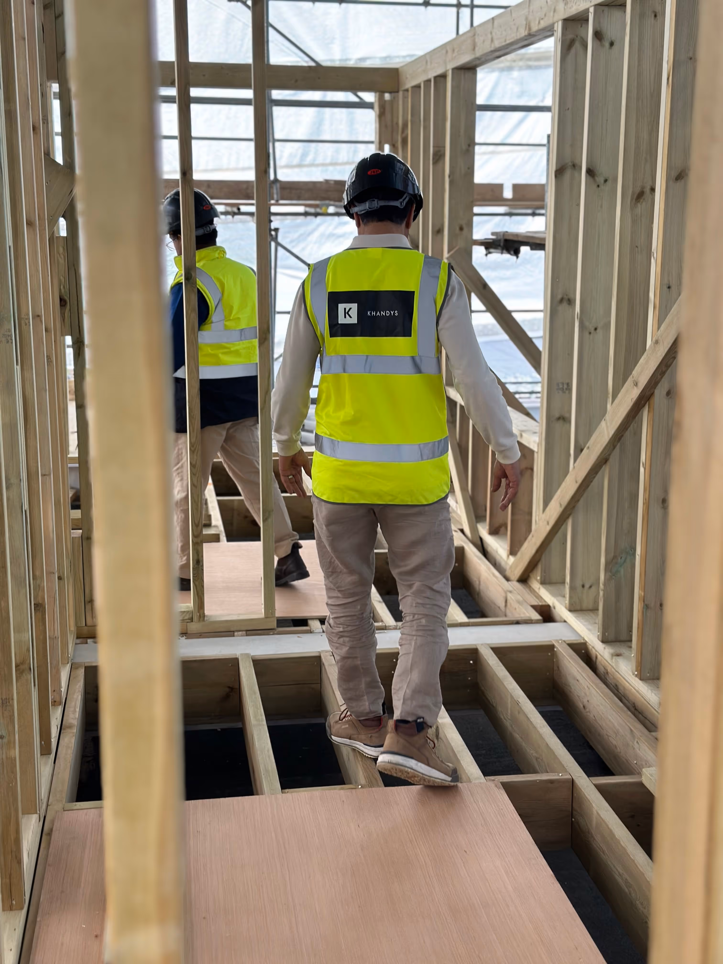 Photo showing the back of a director wearing high visibility jacket with the Khandys logo while walking through a construction site