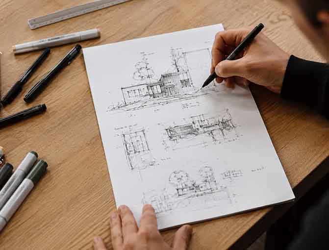 An architects hand holds a pen and draws on some architectural drawings