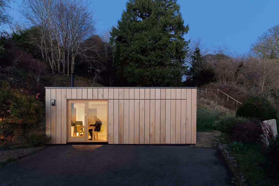An exterior shot of a modern garden studio. A man can be seen working through the window. This was an architectural project in Kent